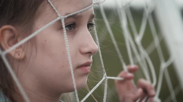 A Sad Girl Looks at the Camera She is Behind a Rope Net