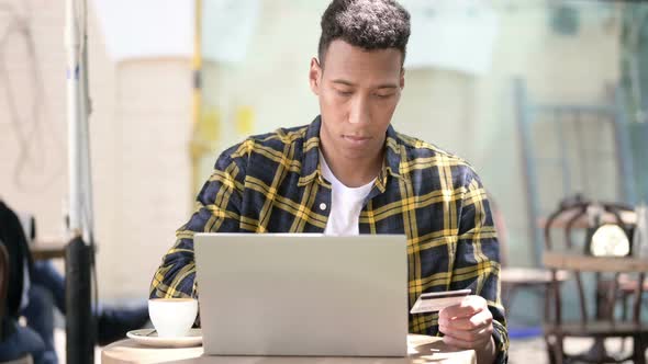 Online Shopping on Laptop By Young African Man, Outdoor Cafe