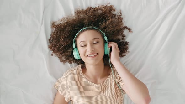 Young Woman Lying on The Bed and Listening to Music