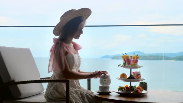 Elegant Lady in White Dress and Straw Hat Pouring Hot Tea and Enjoy Sweet Food