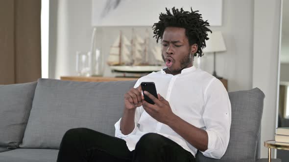 Disappointed African Man Having Loss on Smartphone at Home 