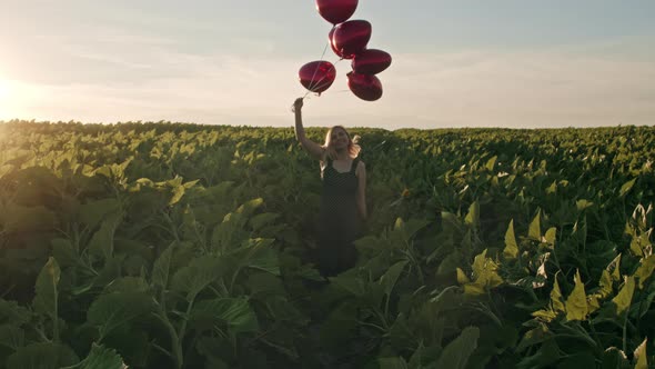 Attractive Woman in Feminine Midi Dress Having Fun with Heart-shaped Balloons on Green Nature