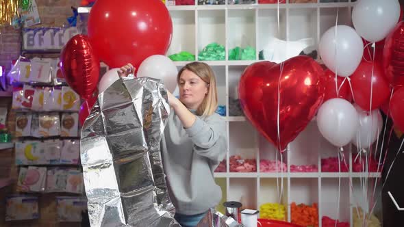a Woman Inflates a Balloon in the Shape of a Large Silver Numeral for a Birthday
