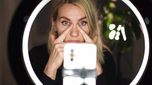 Adorable woman streaming beauty vlog on mobile phone with ring lamp from home