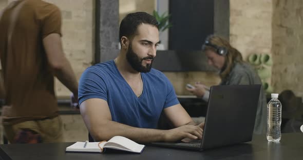 Portrait of Confident Middle Eastern Male Student Typing on Laptop Keyboard with Blurred Friends