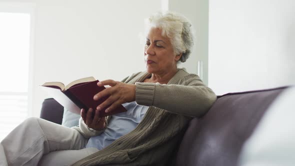 African american senior woman reading a book while sitting on the couch at home