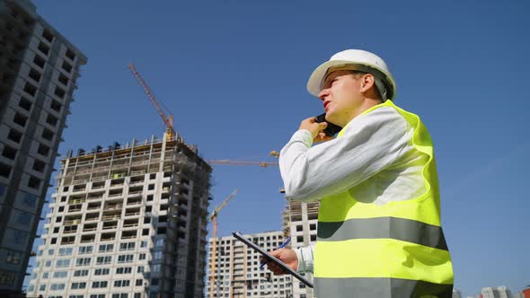 Engineer Talking on Phone and Making Notes at Construction Site