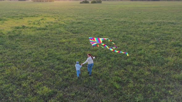 The Mother and Boy Run with a Kite on a Green Field