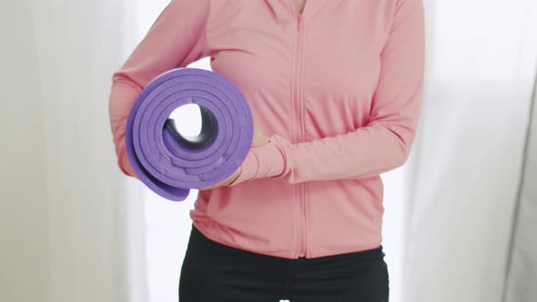 Close-up shot of an attractive young Asian woman holding her yoga mat ready to exercise at home.