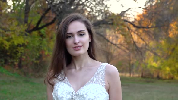 Young Brunette Woman in Long White Dress Walks Along Autumn Colorful Forest.