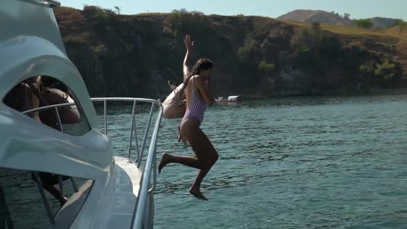 Couple of Girls are Having Fun on a Sunny Day on a Yacht Girls in Bikinis Dive Together From the
