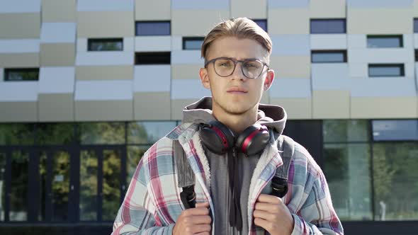 Young Blond Guy Standing On The Street Holding His Backpack Which Is On His Back.