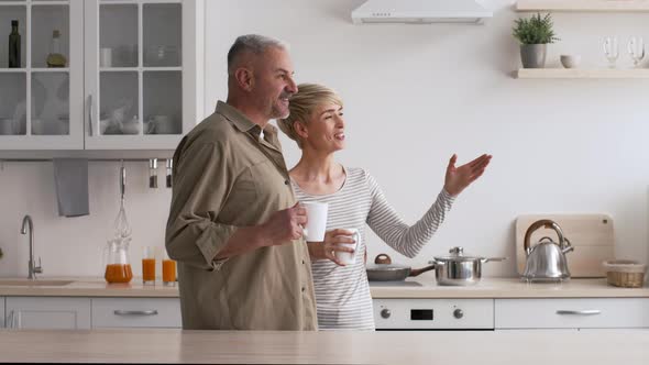 Mature Couple Drinking Coffee Talking Looking Aside In Kitchen Indoor