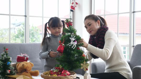 Asian mother and daughter in sweater, decorating christmas tree in living room