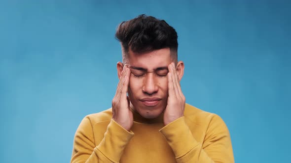 Exhausted and stressed man massaging his head while suffering from headache on an blue background.