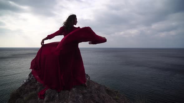 Side View a Young Beautiful Sensual Woman in a Red Long Dress Posing High Above the Sea on a