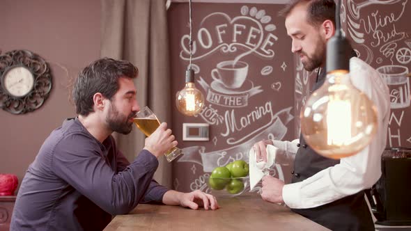 Young Bearded Man Tells a Story To the Bartender and Drinks Beer