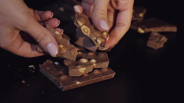 Woman Breaks Black Chocolate Bar with Nuts