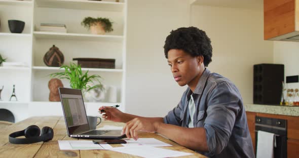 African american man working from home and using laptop and smartphone