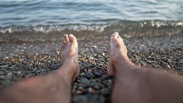 Male Bare Feet are Sunbathing While Sitting on Seashore