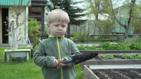 Portrait of a kid with blond hair with a garden shovel in his hands