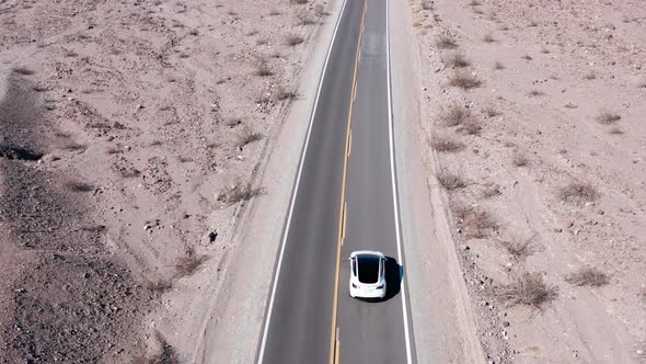 Tesla car on a road traveling down the Death Valley alone. Top down aerial view
