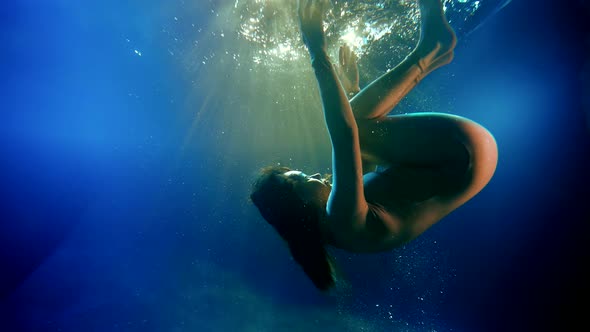 Graceful Brunette is Swimming Underwater Doing Somersaults in Dark Blue Water Dreams and Fantasy