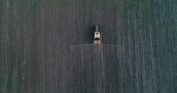 Tractor with trailed sprayer spraying chemicals on agricultural field. Aerial view.