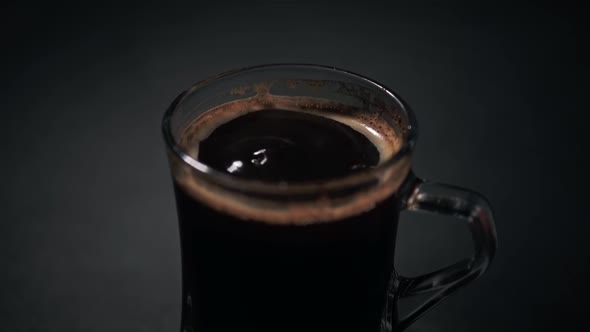 Selective focus close up of drops of black coffee falling inside a cup, isolated caffeine concept ba