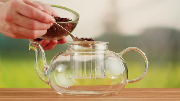 Putting Dry Tea Leaves Into Teapot on a Wooden Table