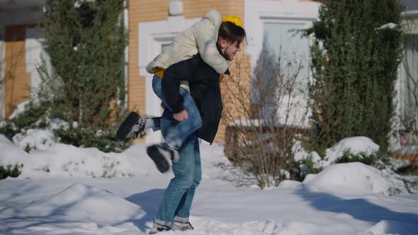 Wide Shot of Happy Laughing Caucasian Boyfriend Holding Girlfriend on Back Spinning in Snow on