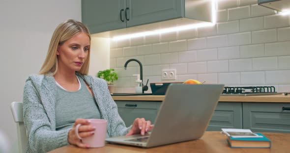 Portrait Shot of the Young Pregnant Mother Sitting at the Kitchen Table and Watching Something