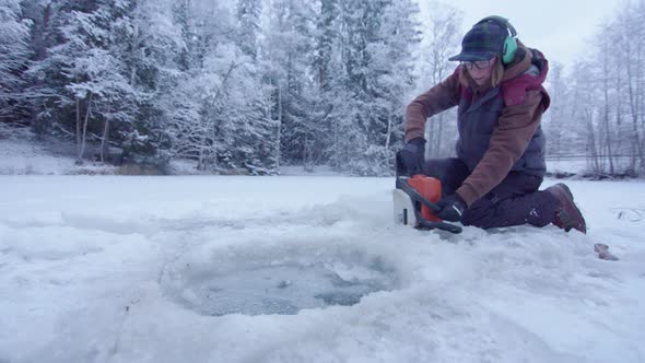 HANDHELD - woman using chainsaw cutting an ice hole