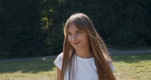 Young Attractive Female Walk and Look at the Camera with Smile on Green Lawn. Cheerfully Young Girl