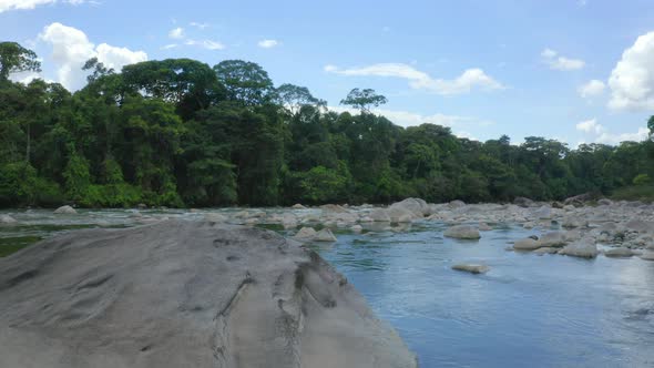 Flying over a large grey colored boulder that is lying in the riverbed