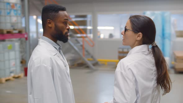 Diverse Workers in White Coats Inspecting Chemical Factory Warehouse