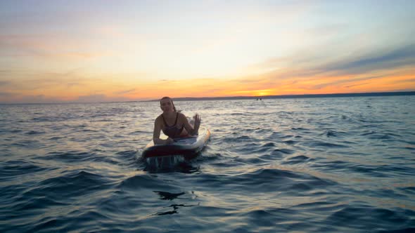 Young Woman Is Lying on a Paddleboard in the Open Water During Sunset