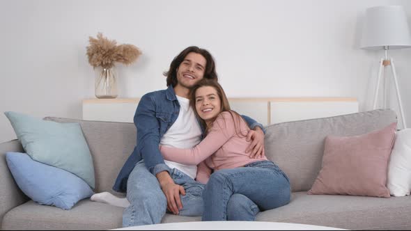 Happy Millennial Couple in Love Spending Time Together at Home Embracing on Couch and Laughing