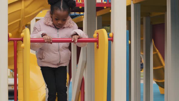 African American Girl Alone Plays in Playground Child Climbs Steps and Slide Down Jumping Childrens