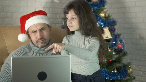 Father with child in Santa hat by computer in room.