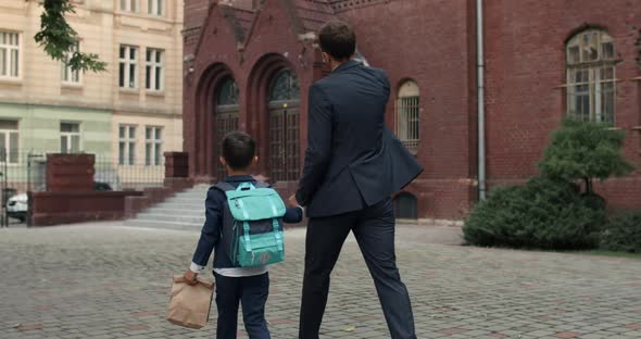 Backside View of Dad in Suit and His Little Son with Bag Going To School at First Day, Father