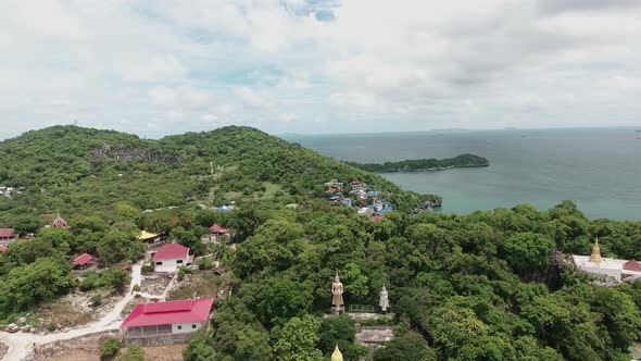Descending aerial view over large Buddha sculpture among tropical green island landscape. Koh Si Cha