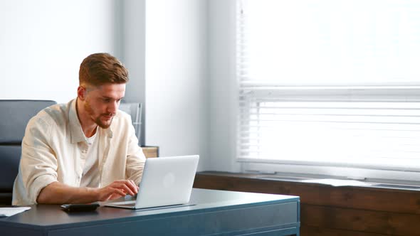 Concentrated man manager in yellow shirt types on white laptop