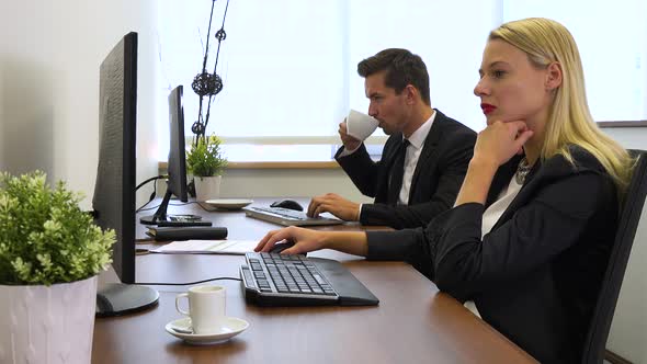 Two office workers, man and woman, work on computers