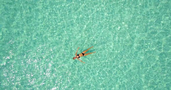 Aerial drone view of a woman floating and swimming on a tropical island.