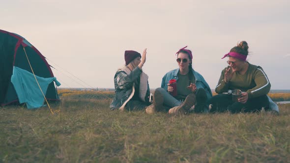 Girl Friend Tourists Rest Talking on Grass By Tent at Sunset