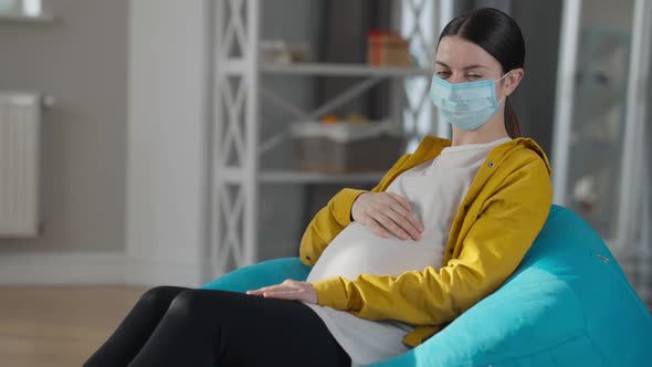 Portrait of Happy Young Woman in Covid Face Mask Caressing Pregnant Belly Smiling Looking at Camera