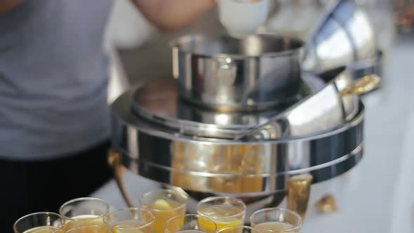 Glasses Filled with Orange Juice and Alcohol and Waitress Girl Pouring Punch with Ladle Into Glasses