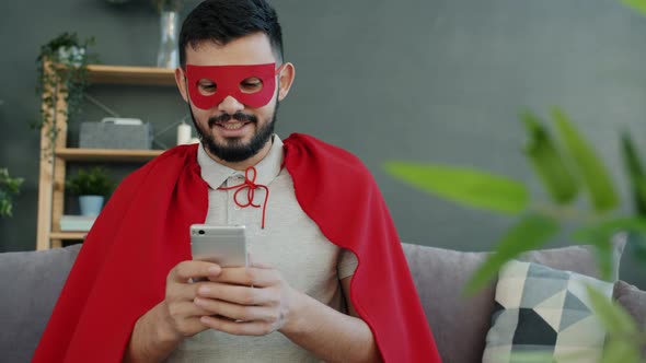 Excited Man in Red Cape and Mask Using Smartphone Enjoying Good News Online