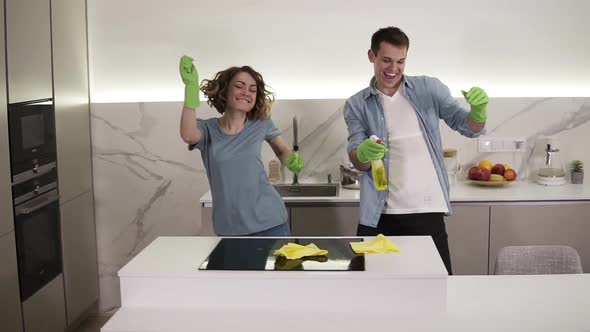 Happy Young Couple Dancing in Kitchen Both in Green Rubber Gloves Having Fun on Cleanup Day in